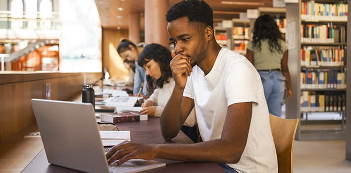 Male student using a laptop in a library.