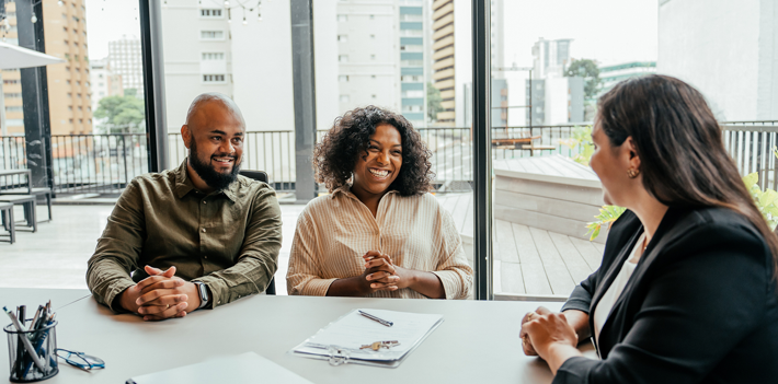 Three individuals are seated at a table in an office setting.