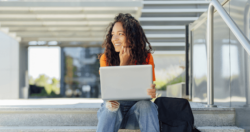 Smiling-student-sitting-with-laptop-on-steps-in-campus