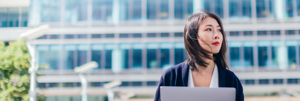 A woman uses her laptop outside a building.