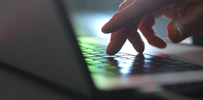 Hands touching laptop keyboard in dark at home office