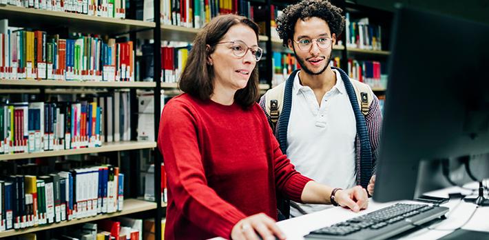 A librarian helps a student locate a book using a computer.