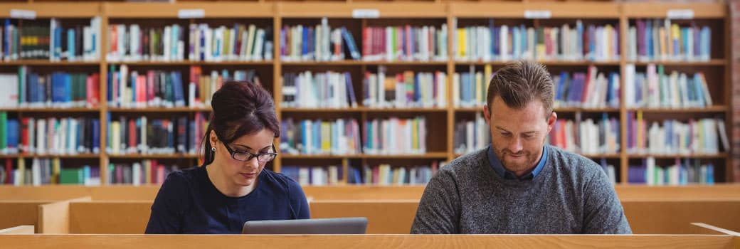 Two researchers sit in a library in front of bookshelves