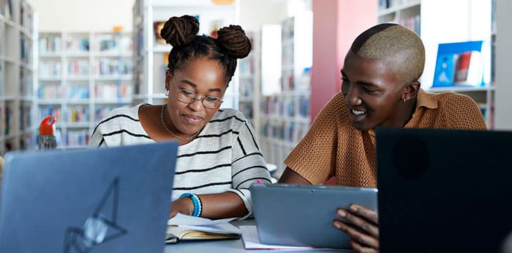 Students sitting at a library desk with laptops.