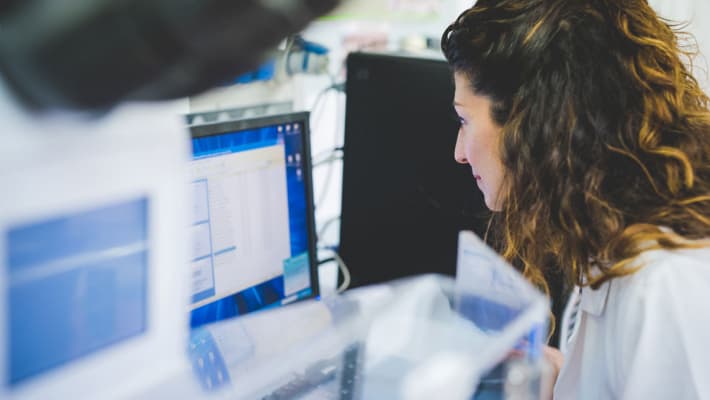 Researcher in a white coat looks at a computer screen