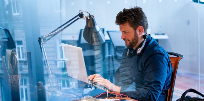 Focused male computer programmer working on laptop at desk in office